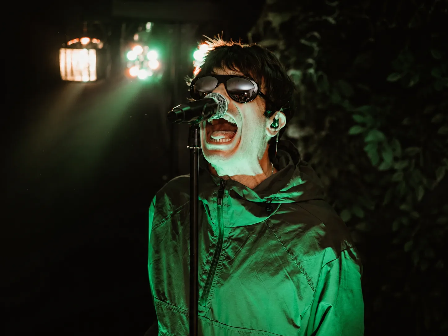 Liar Gallagher singing live into a microphone under green stage lighting